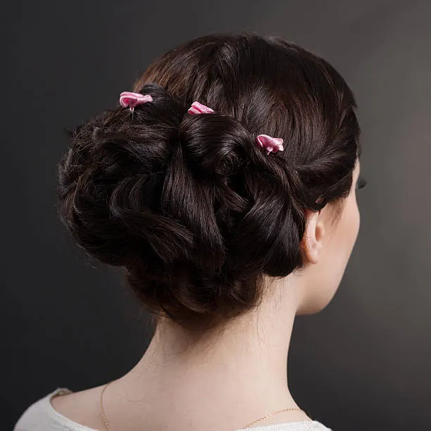 Elegant side profile of a bride with a sleek classic French twist, straight brunette hair, small pearl pins, soft studio lighting against a neutral cream background.