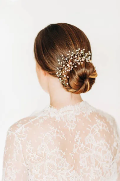 Portrait of a bride with a soft twisted crown updo creating a halo effect, loose tendrils, wavy hair, soft natural light against cream background.