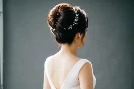 Back view of a bride with a voluminous bridal bun, extra height and fullness, dramatic but elegant, soft studio lighting with neutral background.
