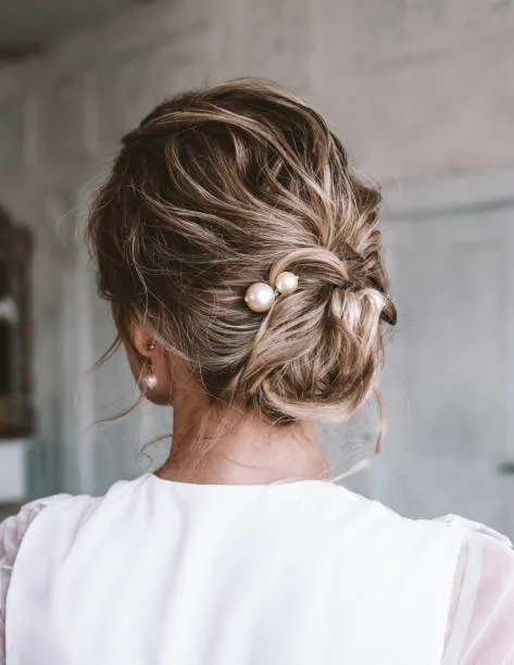 Side profile of a bride with a vintage glam chignon, polished waves combined with sophisticated low bun, vintage-inspired gown, cathedral veil, heirloom jewelry, warm studio lighting.