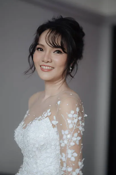 Three-quarter view of a bride with a soft glam bridal updo, gentle volume, relaxed curls, subtle shine, polished yet approachable, soft studio lighting.