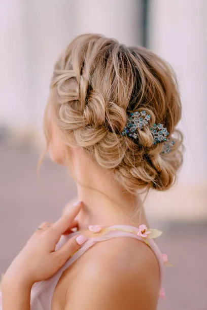 Side profile of a bride with a romantic side chignon placed gently below one ear, soft curls framing face, one-shoulder dress, soft window light in elegant interior.