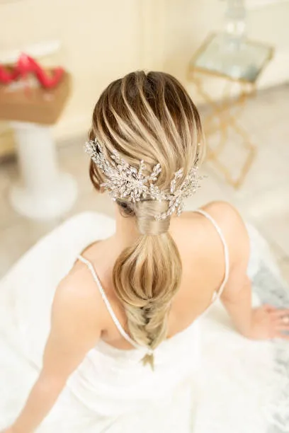 Side profile of a bride with a royal tiara updo, delicate tiara paired with elegant low bun, regal appearance, formal ballroom setting with chandelier light and luxurious background.
