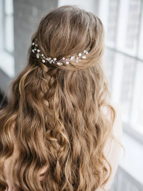 Side profile of a bride with a romantic curly chignon, naturally curly hair pinned into soft voluminous shape, warm skin tone, golden hour outdoor light in garden setting.
