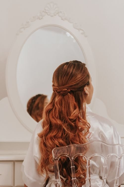 Free A redhead woman sits in front of a mirror, showcasing her elegant braided hairstyle. Stock Photo